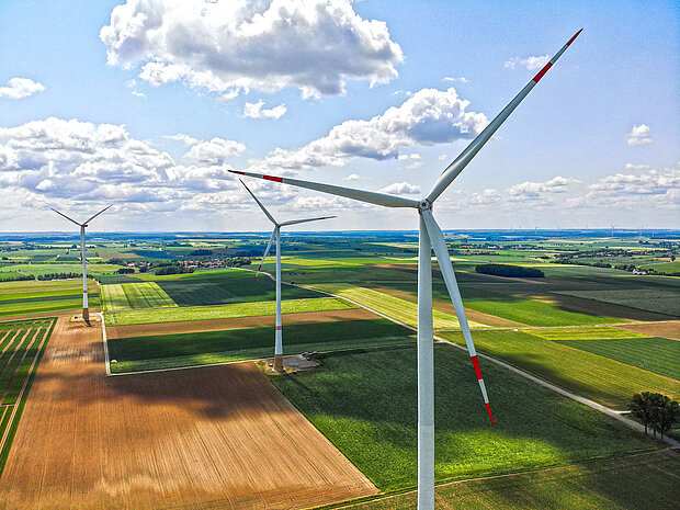 Luftaufnahme von drei Windrädern über einer Agrarlandschaft.