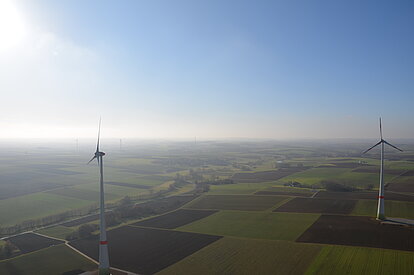 Weite Agrarflächen mit modernen Windrädern prägen das Landschaftsbild des Bürgerwindparks Gollhofen-Rodheim bei klarem Himmel.