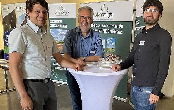 Drei Personen im Gespräch an einem Stehtisch beim Netzwerktreffen in Ansbach – im Hintergrund Banner von N-Ergie und ökenergie mit Fokus auf regionale Partnerschaften für erneuerbare Energien.