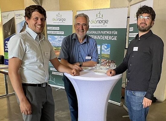 Drei Personen im Gespräch an einem Stehtisch beim Netzwerktreffen in Ansbach – im Hintergrund Banner von N-Ergie und ökenergie mit Fokus auf regionale Partnerschaften für erneuerbare Energien.