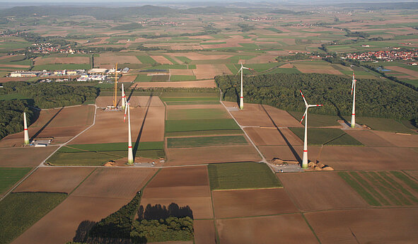 Windenergieanlagen des Bürgerwindparks Gollhofen-Rodheim stehen verteilt über landwirtschaftlich genutzte Flächen mit Blick auf benachbarte Ortschaften und sanfte Hügel im Hintergrund.